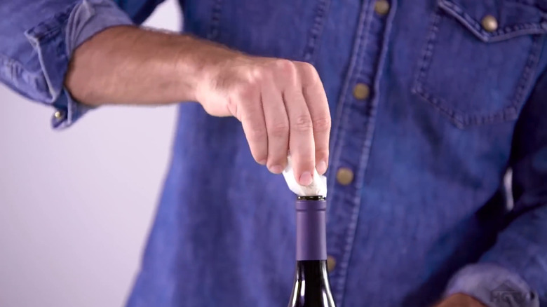 Hand re-corking a wine bottle with wax paper-wrapped cork