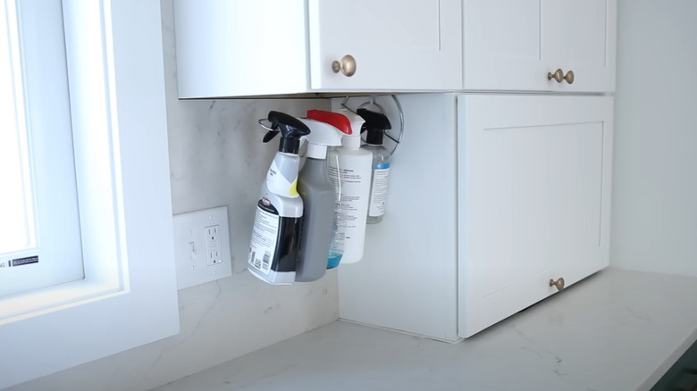 Bottles hanging from a mounted paper towel holder under a cabinet.