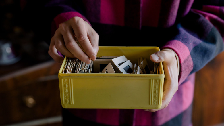 A person wearing a buffalo plaid shirt holds a yellow recipe box full of photo slides