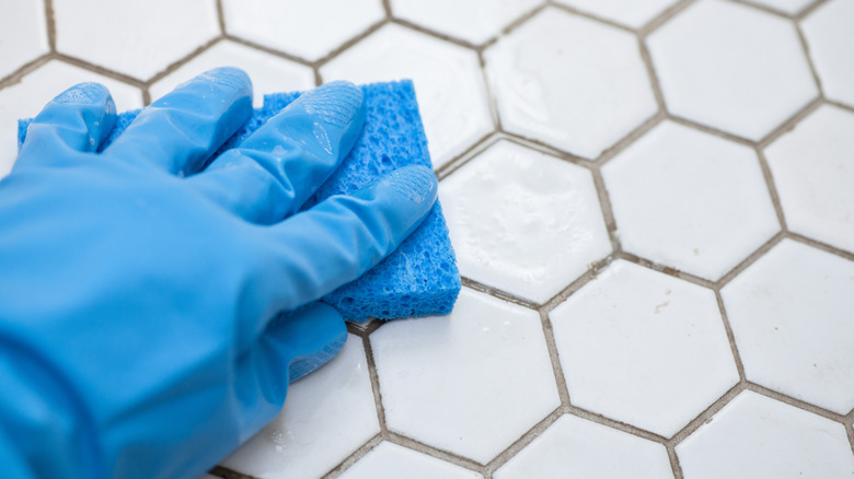 Gloved hand cleaning tile floor grout with a sponge