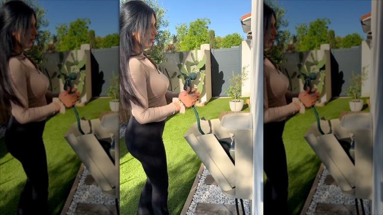 A woman puts a green hose into a gray wall-mounted organizer