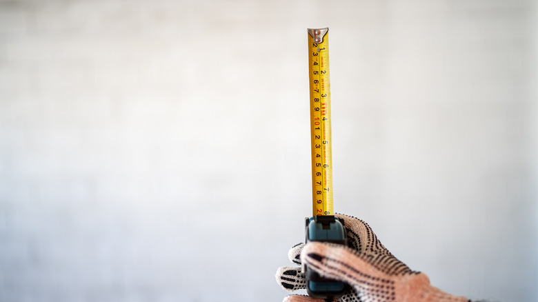Someone holding a tape measure in front of a blank wall