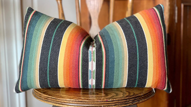 A throw pillow covered in a vintage Southwestern Serape-style saddle blanket cover sits on a wooden chair