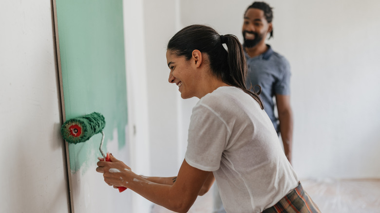 A young couple smiles while painting a room sea foam green