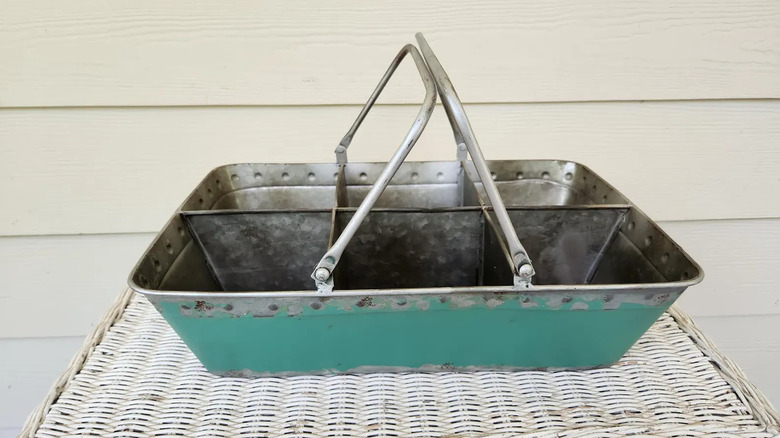 A vintage metal silverware caddy sits on top of a white wicker table