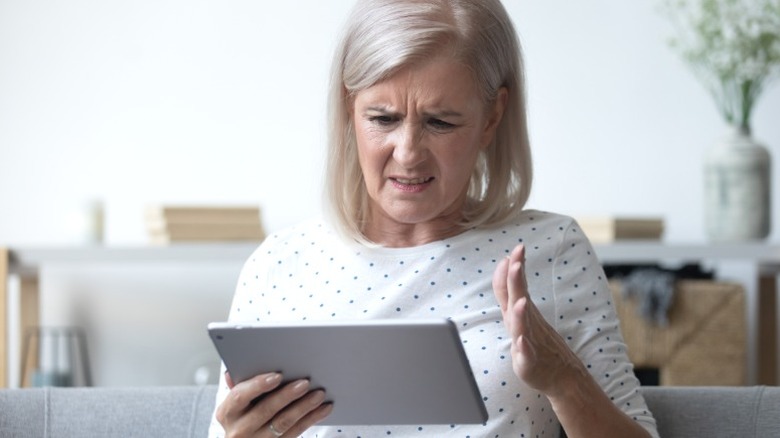Frustrated woman looking at tablet at home