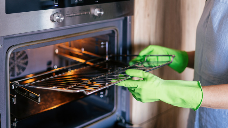 Gloved hands removing dirty racks from a built-in oven