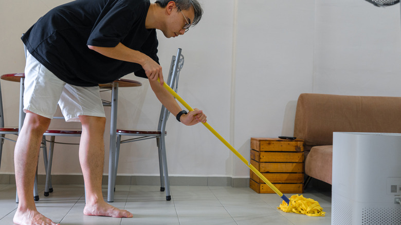 Man mopping a tiled floor with a yellow mop