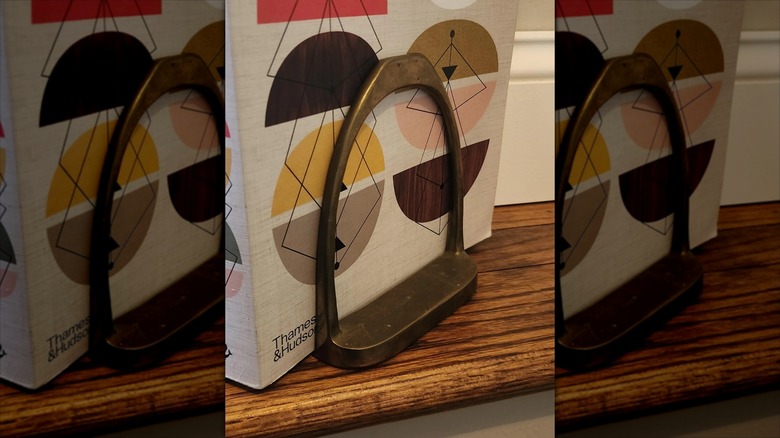 A vintage brass stirrup has been repurposed as a bookend