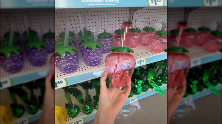 a hand holding a strawberry-shaped plastic tumbler at Dollar Tree
