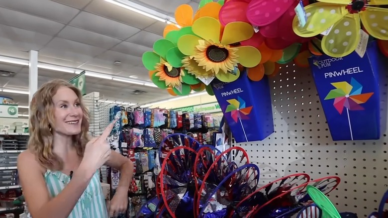 a woman points to a sunflower pinwheel in a basket