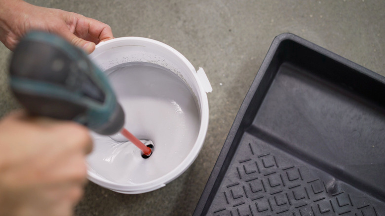 Person mixing paint with a drill attachment