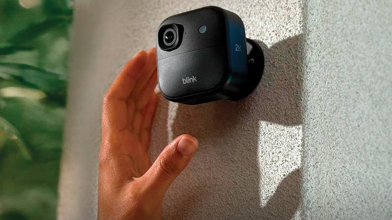 hand reaching for Blink camera mounted on a wall
