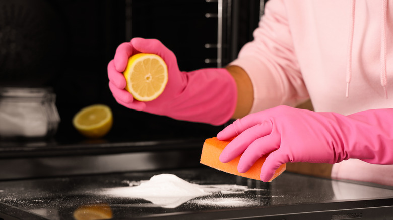 Man with sponge, wearing gloves, cleaning oven with lemon and baking soda