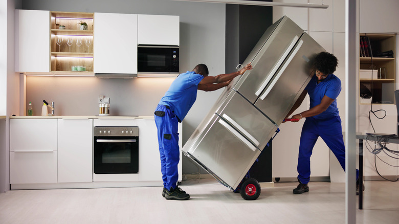 Two people moving a refrigerator in a kitchen