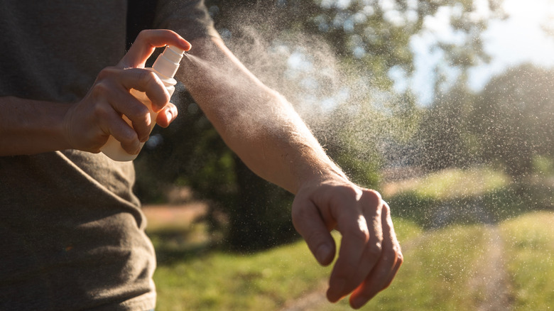 Person applying insect repellent spray on arm