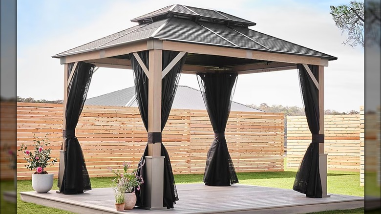 A large patio gazebo is surrounded by a light wooden fence