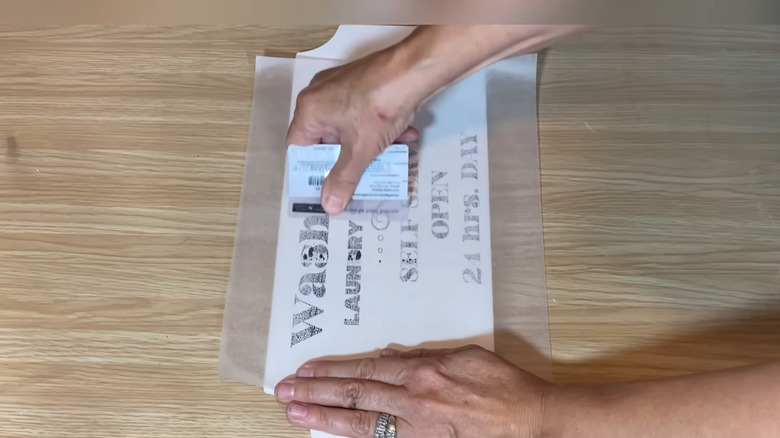 Hands pressing ink transfer wax paper onto wooden sign