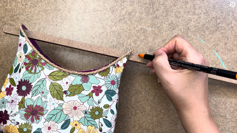 Creator marking the length on a wood bar attached to a flower-themed container made out of a laundry detergent bottle