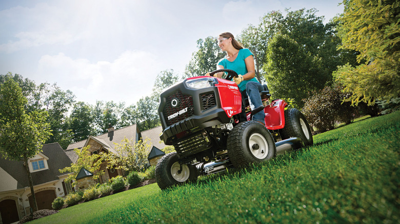 A woman using the Troy-Bilt Pony 42-inch 547cc 7-speed gas riding mower on a lawn