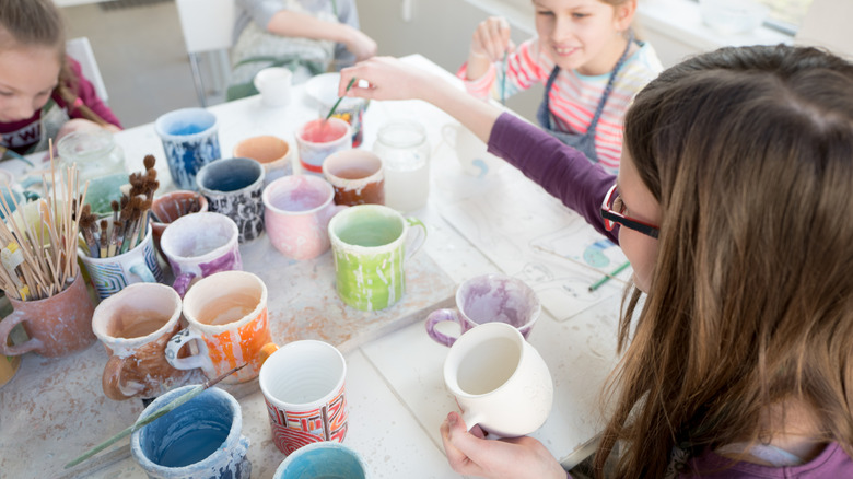 Kids painting at craft table with brushes and coffee mugs
