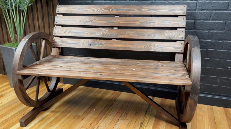 A large wagon wheel wooden bench sits in front of a black brick wall