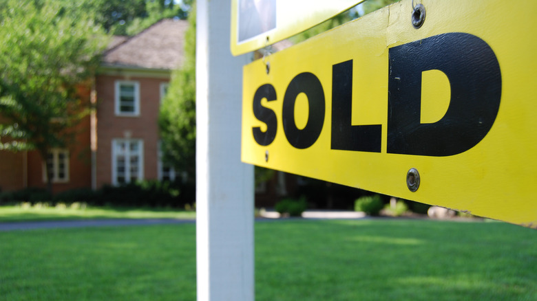 Colonial style home in the backdrop of a for sale sign